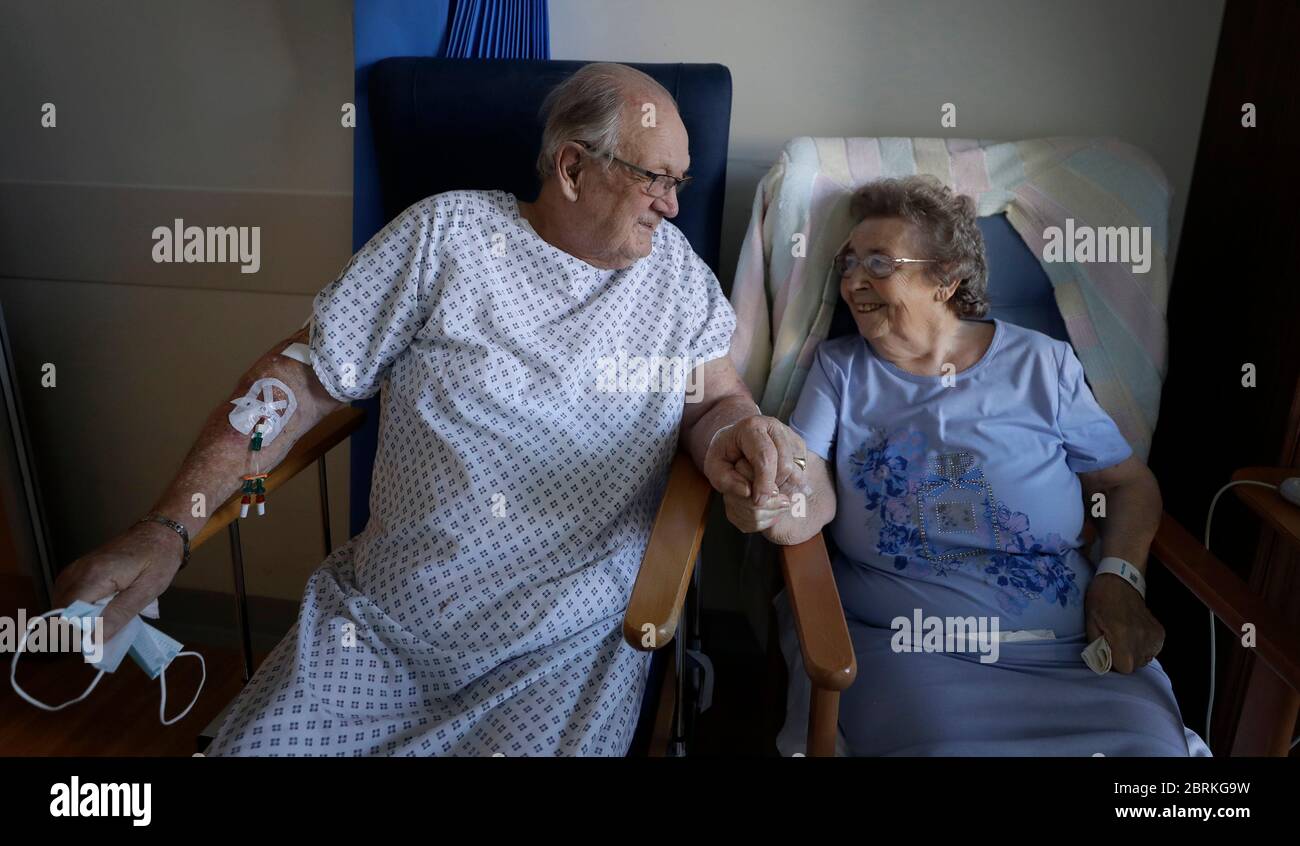 Coronavirus patients George Gilbert, 85 and his wife Domneva Gilbert 84, hold hands during a short visit, they are being treated in different areas, and both are part of the TACTIC-R trial, at Addenbrooke's hospital in Cambridge. Stock Photo