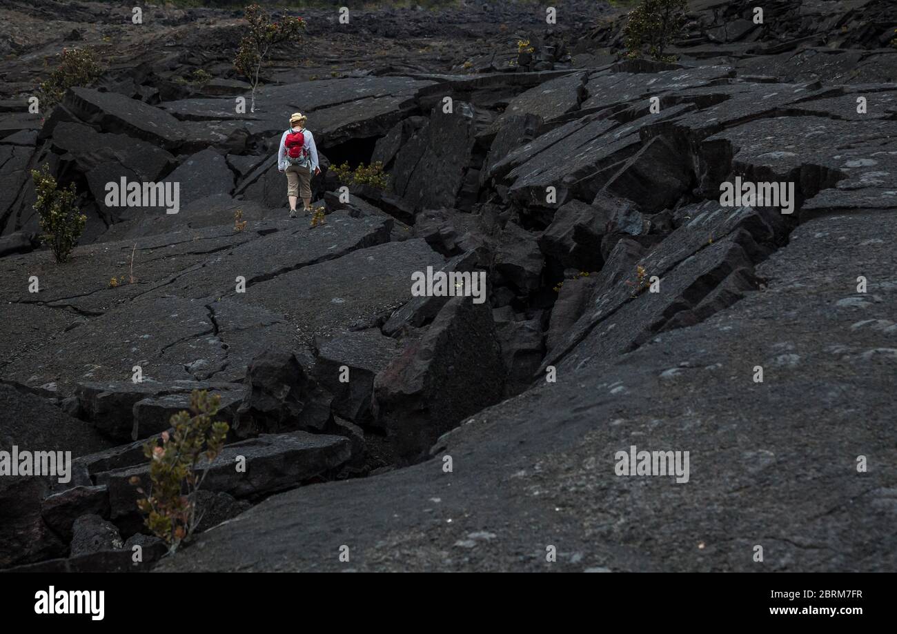A woman stands on the cracked and fallen in lava of floor of Kilauea