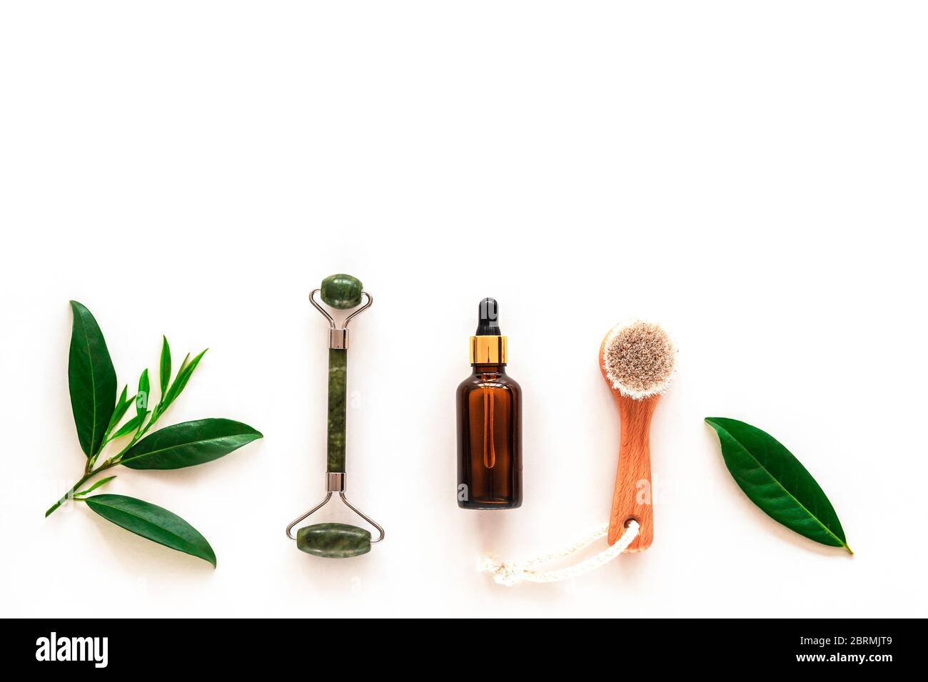 Ingredients for natural beauty treatment. Oil made of herbs, face roller and wooden brush, top view, flat lay, copy space. Stock Photo
