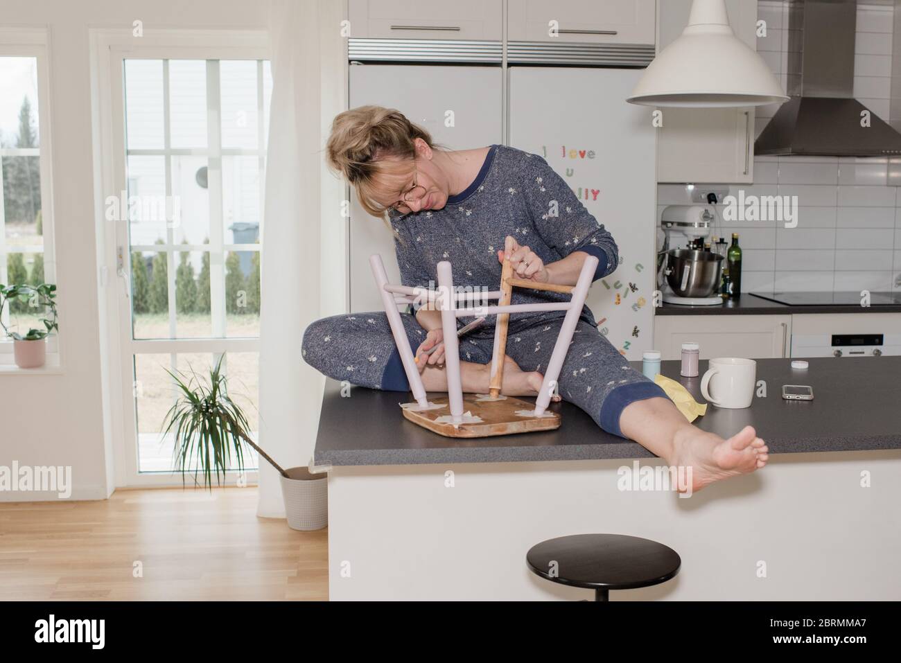 woman sat at home painting a stool in the kitchen Stock Photo
