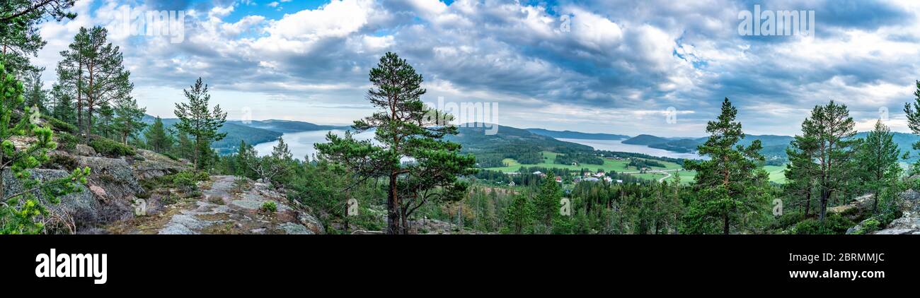 Very wide panorama over wild Scandinavian mountains with pine tree forest, the village and two sea bays, summer day with heavy dramatic clouds, North Stock Photo