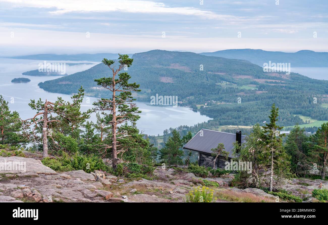 Public tourist rest house in front of view over Scandinavian mountains with pine tree forest, the village and two sea bays, summer day with heavy dram Stock Photo