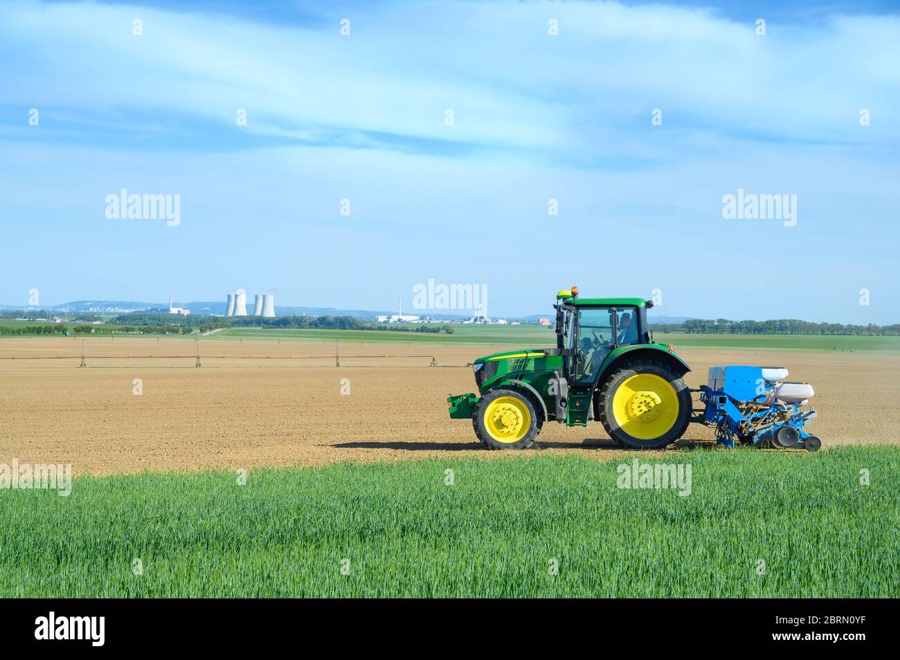 Tractor sowing crops at grain field, blue sky Stock Photo