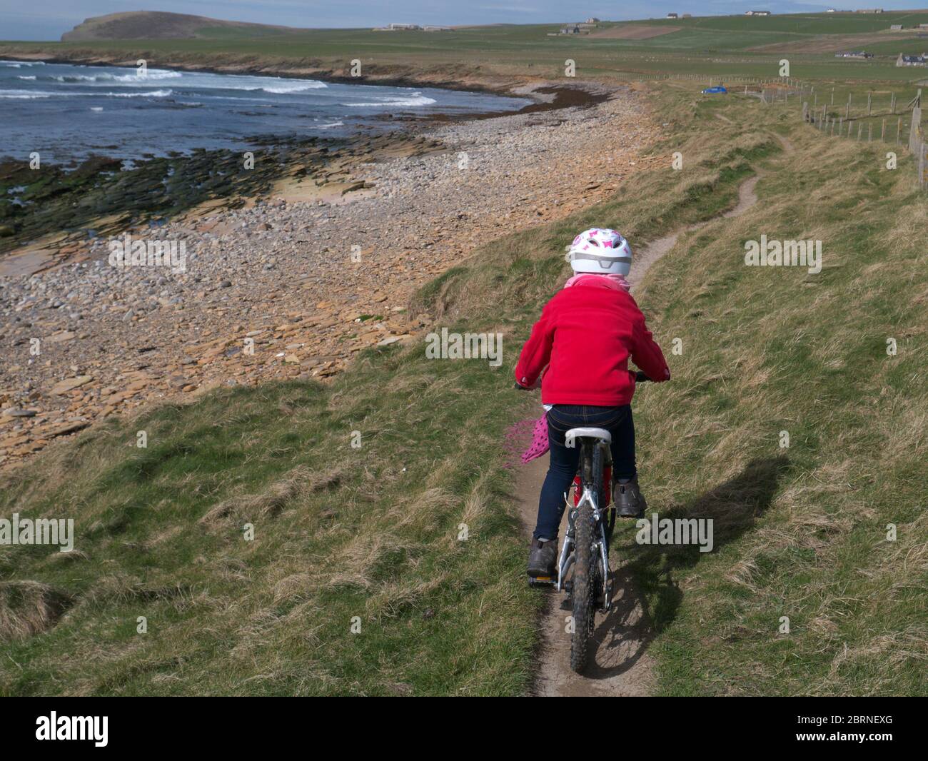Young girl cycling on coastal path, Orkney Isles Stock Photo