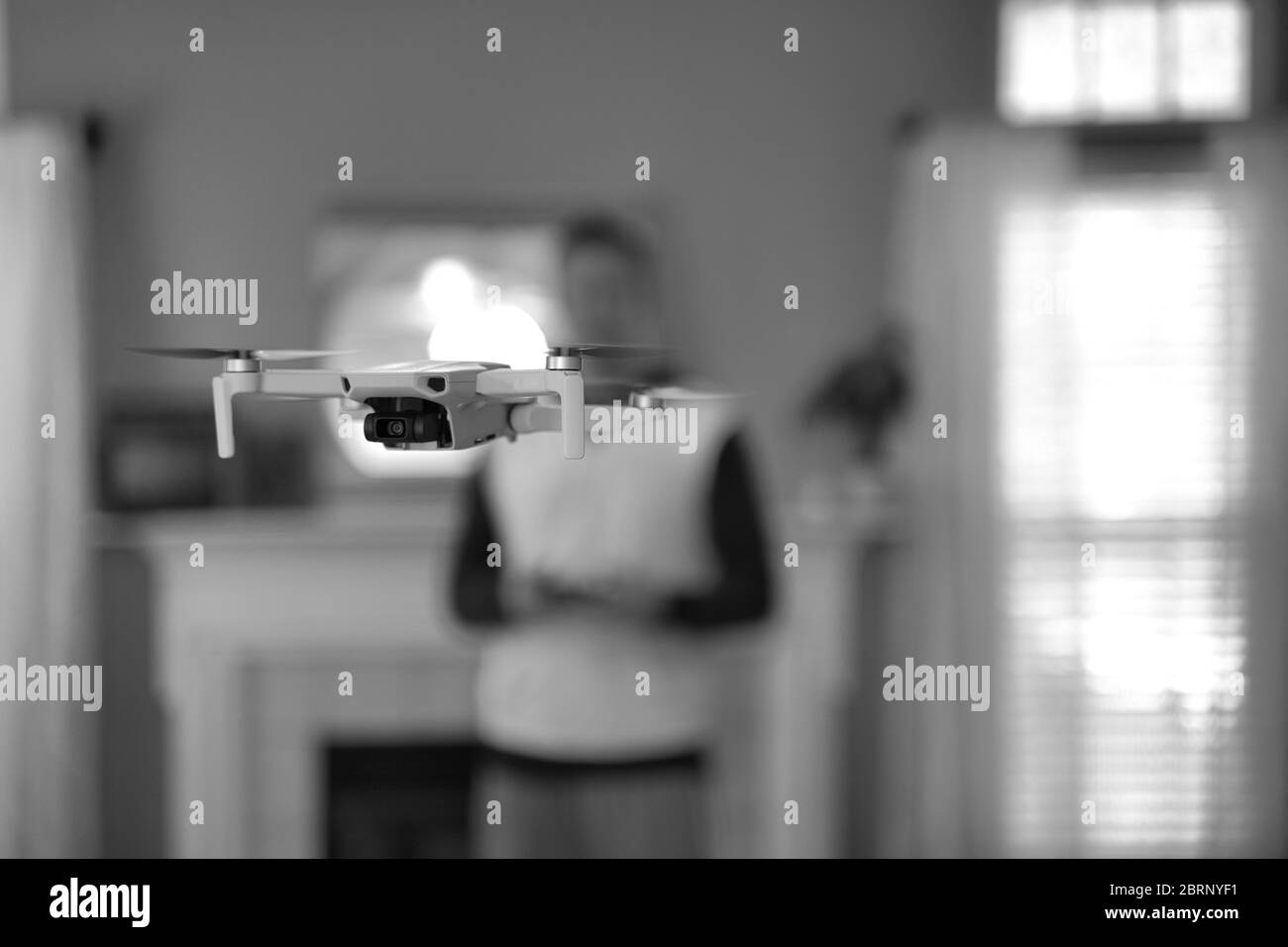 Drone flying indoors with pilot visible in background. Amateur drone flight. User wearing sweatshirt flying drone inside of home on cold day. White dr Stock Photo