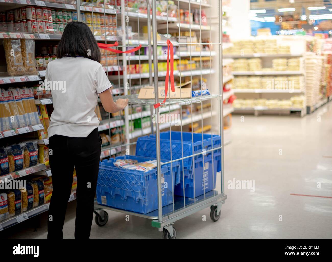 BANGKOK / THAILAND: MAY 15 - 2020: The employer wear surgical mask and uniform pushing cart the tray of goods at the supermarket aisle prepare to shop Stock Photo