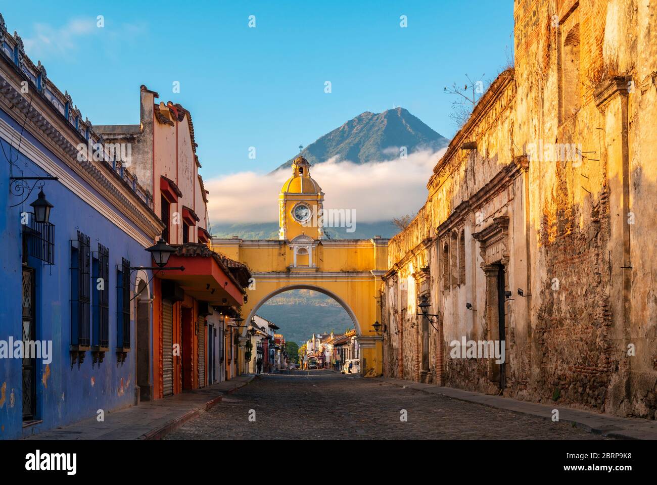 The Santa Catalina Arch in the Main Street of Antigua City without people and the Agua Volcano in the background at sunrise, Guatemala. Stock Photo
