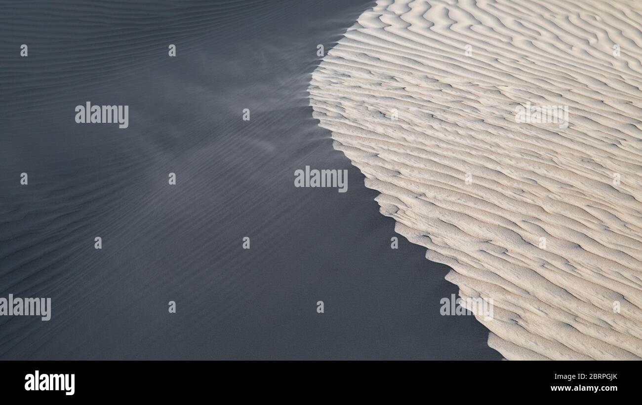 Wind blowing sand at the top of a sand dune. Abstract image, showing light and dark sides Stock Photo