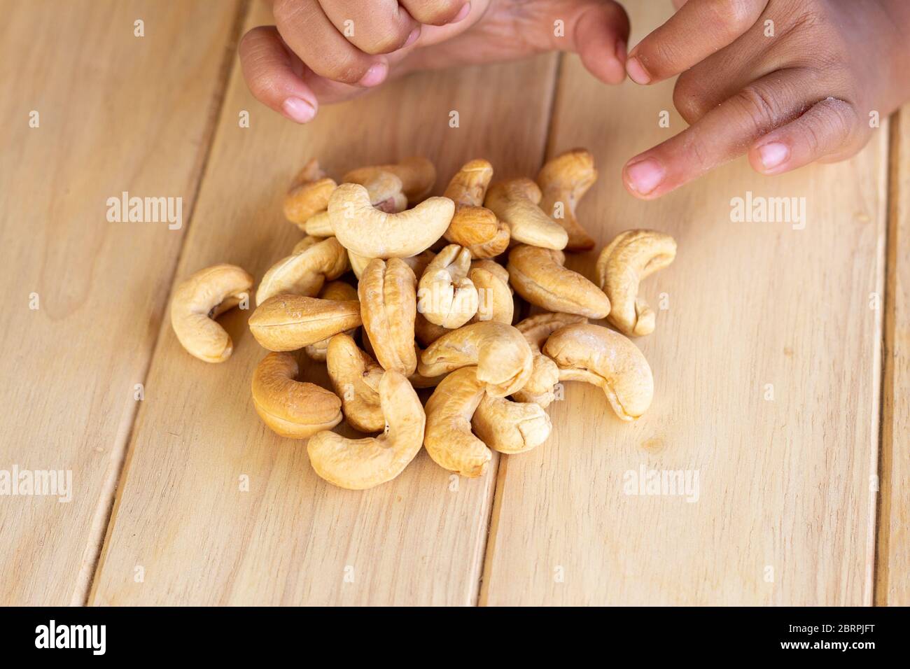 Many Roasted salted cashew nuts  and kid hand on wooden background Stock Photo