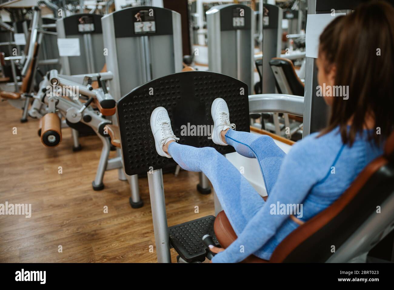 An attractive young caucasian girl in blue sports equipment on a leg machine in the gym Stock Photo