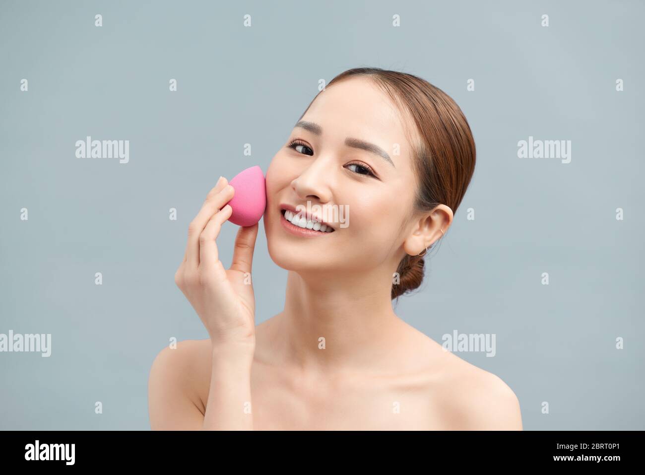 Beautiful young woman applying makeup using beauty blender sponge. Stock Photo