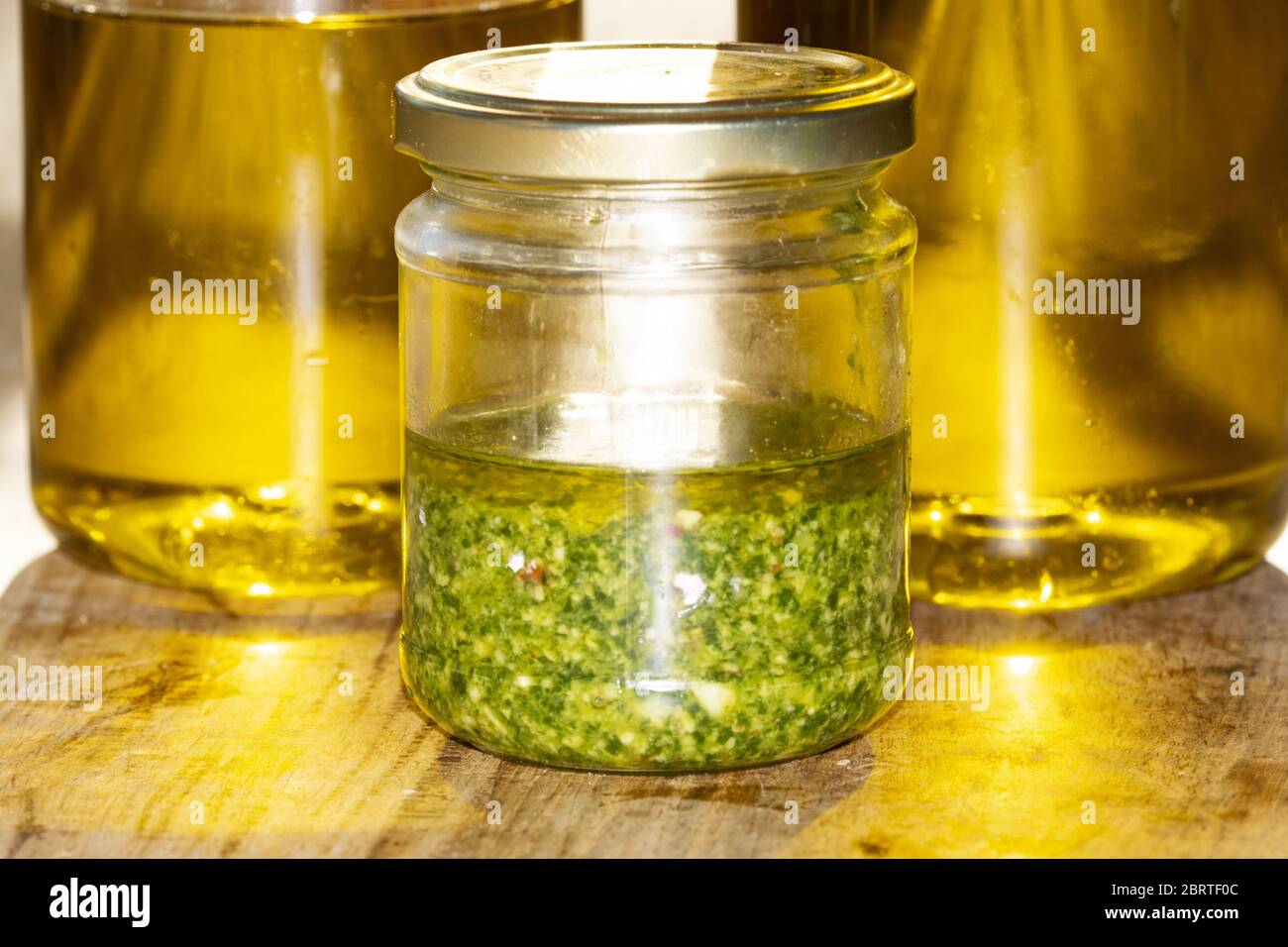 handmade basil pesto in a glass jar near some oil bottles Stock Photo