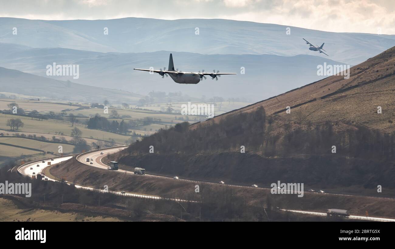 A pair of Royal Air Force Lockheed C130 Hercules transport military aircraft flying low level over the M6 motorway in Cumbria near Tebay. Stock Photo