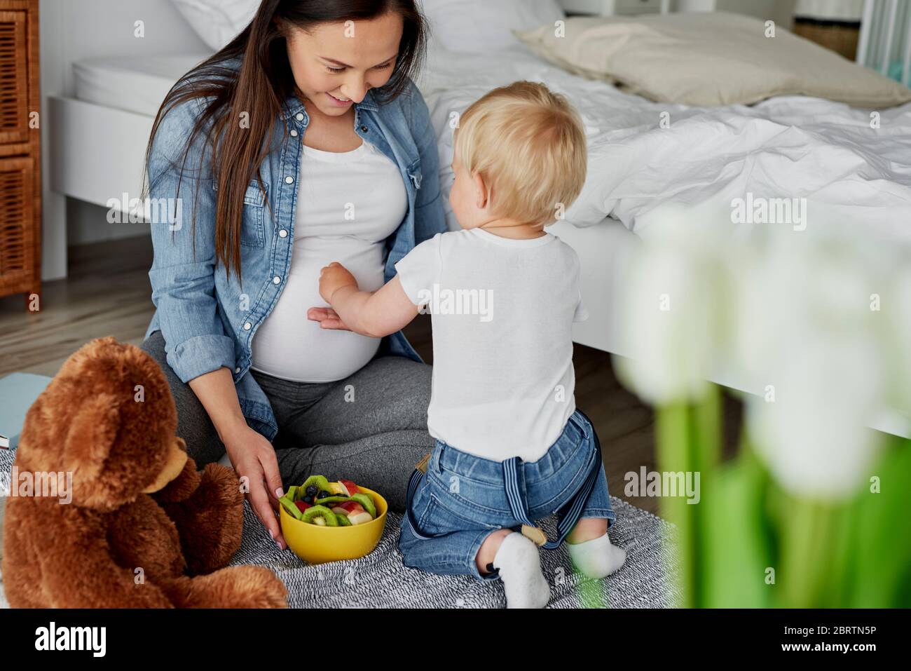 Little brother feeding with fruits his future sibling Stock Photo