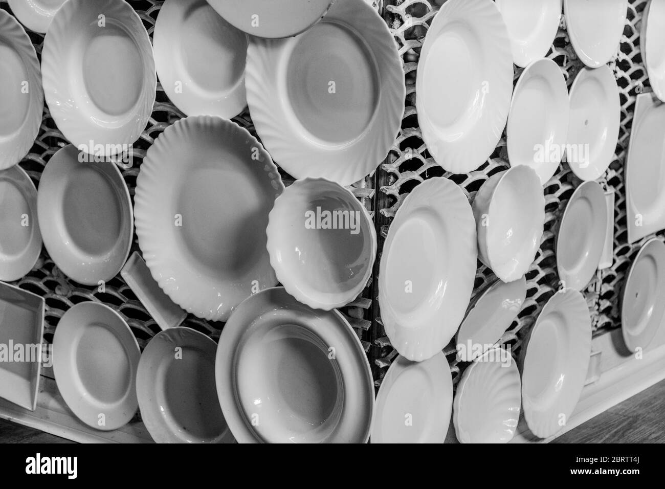 Black and white photography of white crockery plates and dishes are displayed on white lattice wall. Dinnerware of different sizes Stock Photo