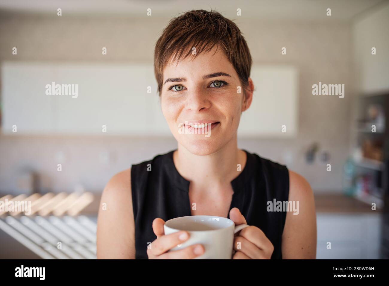 Front view of young woman with coffee standing indoors at home. Stock Photo