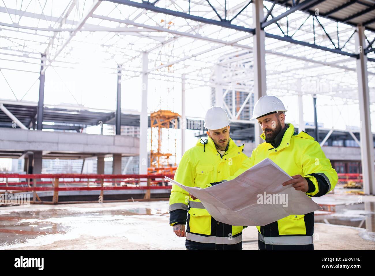 Men engineers standing outdoors on construction site, holding blueprints. Stock Photo
