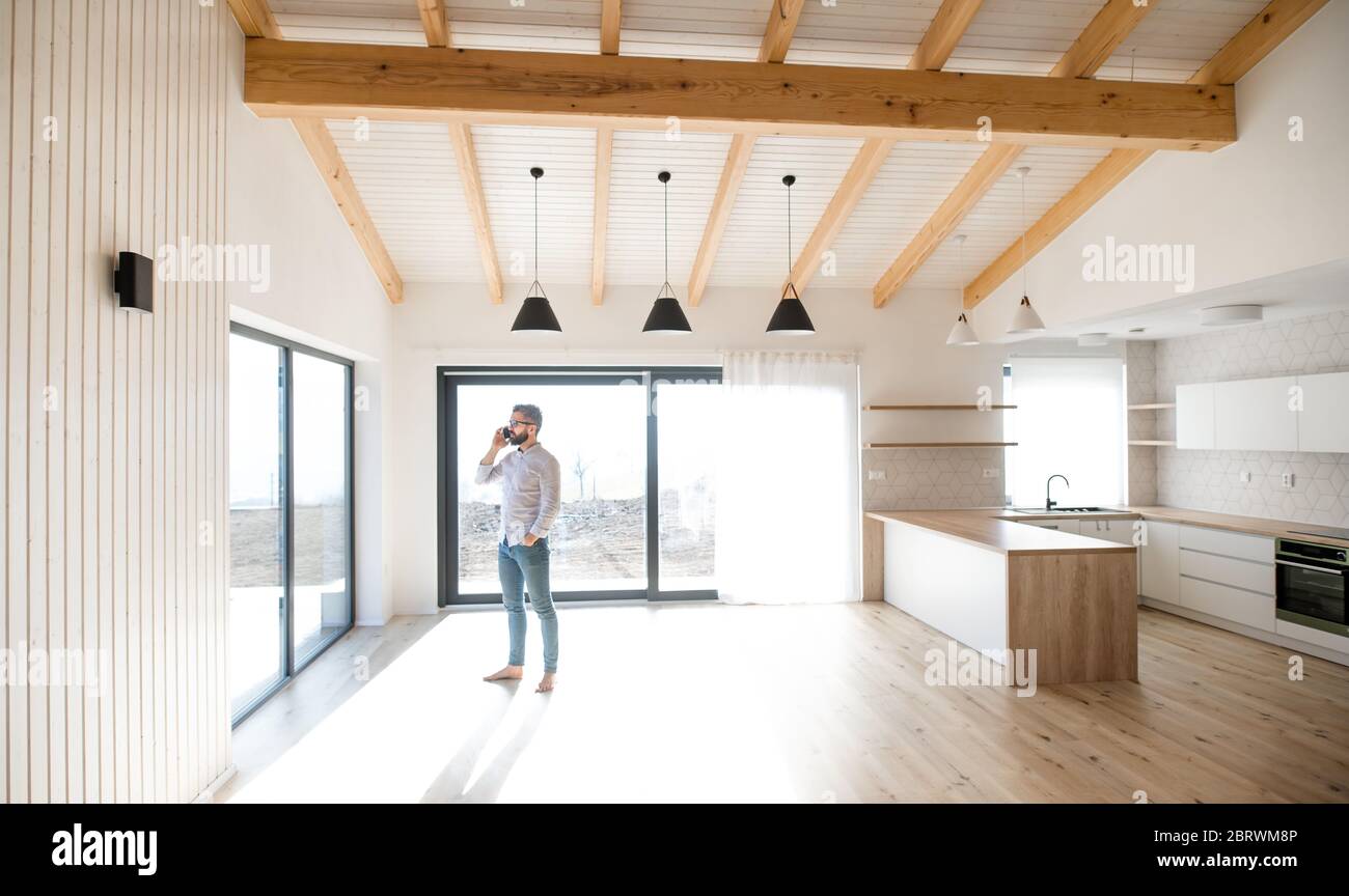Mature man standing in new house, using smartphone. Stock Photo