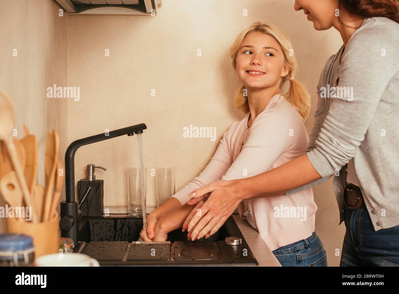 Selective focus of smiling kid washing hands near mother in kitchen Stock Photo