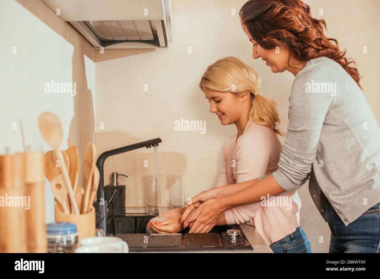 Side view of smiling mother and kid washing hands in kitchen Stock Photo