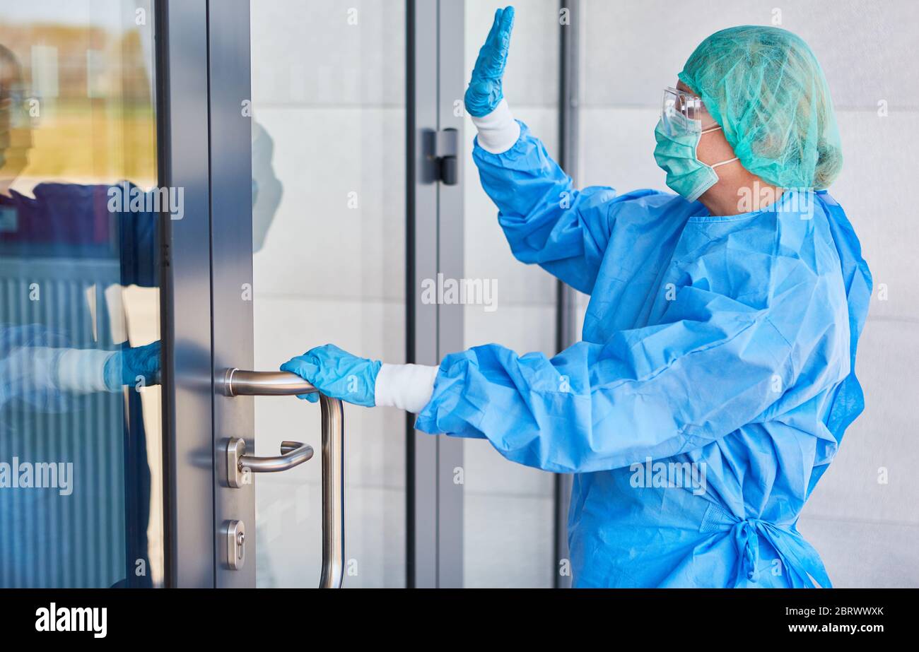 Surgeon in protective clothing in front of clinic makes hand signals at the door to the entrance to the Covid-19 pandemic Stock Photo