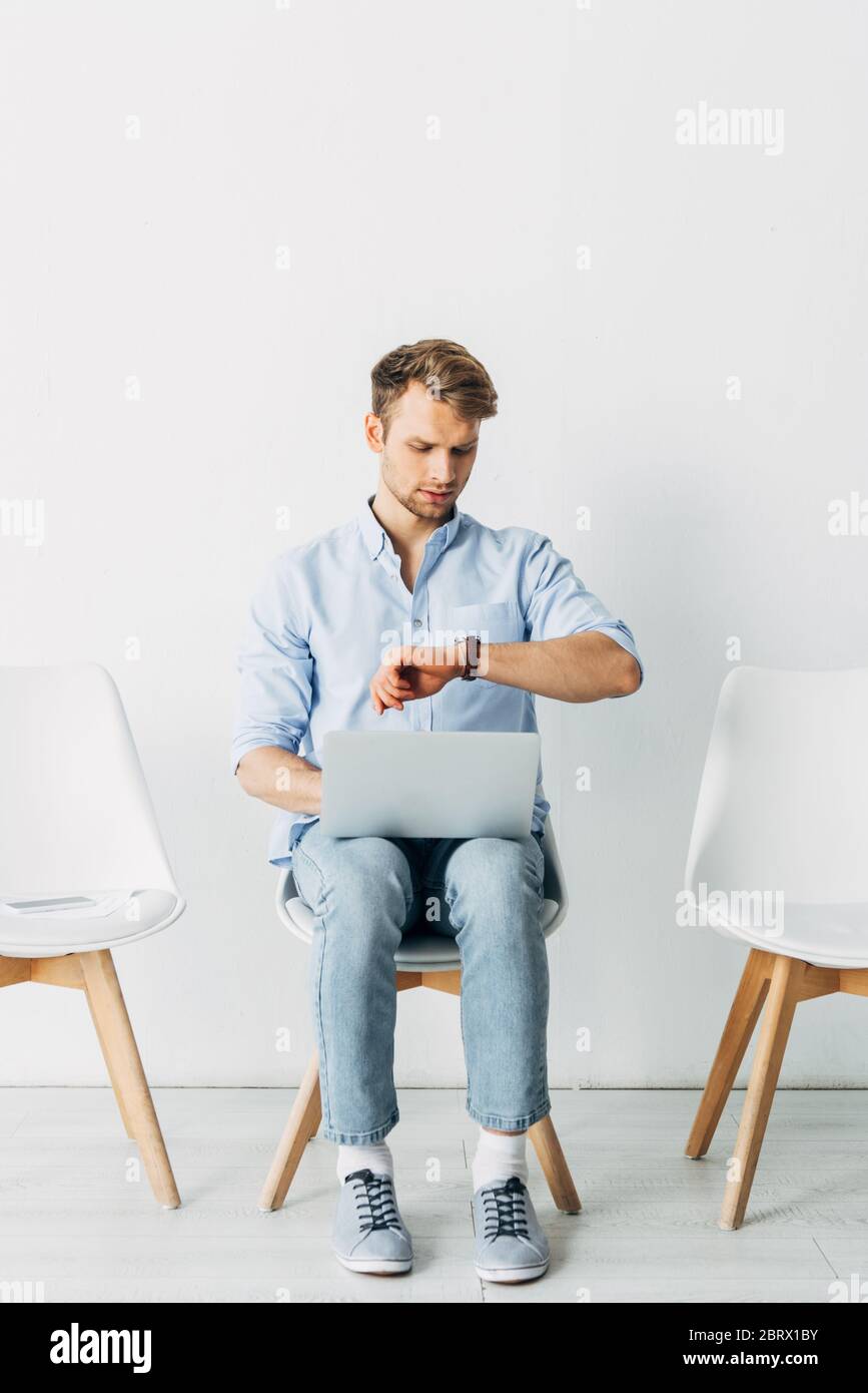 Employee with laptop looking at wristwatch in office Stock Photo - Alamy