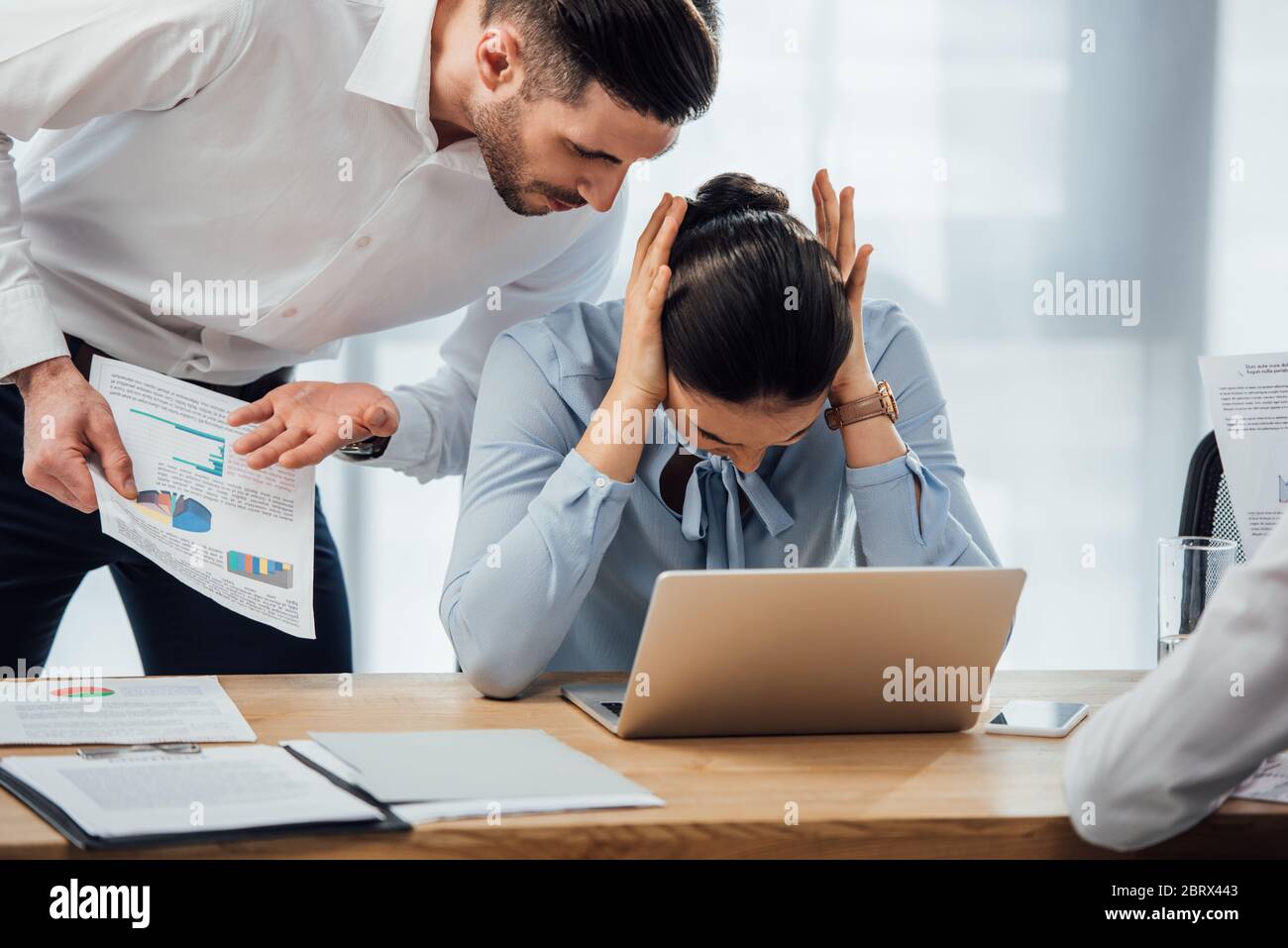 Selective focus of businessman pointing at papers near mexican colleague cowering ears in office Stock Photo