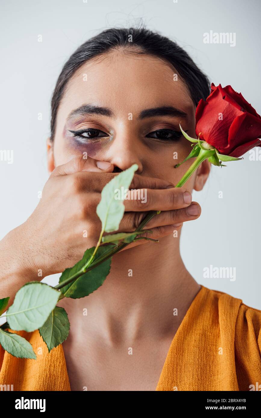 Male hand covering mouth to indian woman with bruise while holding rose ...