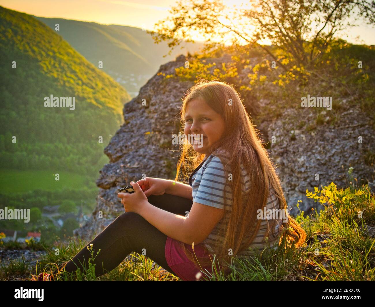 A young girls sits in a squat infront of a large rock. Stock Photo