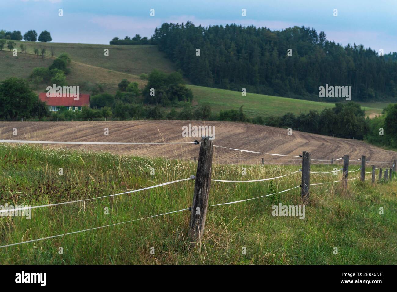 Electrified fence surrounding a farmland with agricultural fields, and a house, in the wooded hills near Schwabisch Hall town, Germany, at dawn. Stock Photo