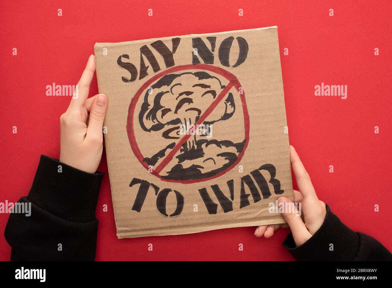 partial view of woman holding cardboard placard with say no war to war lettering and explosion in stop sign on red background Stock Photo