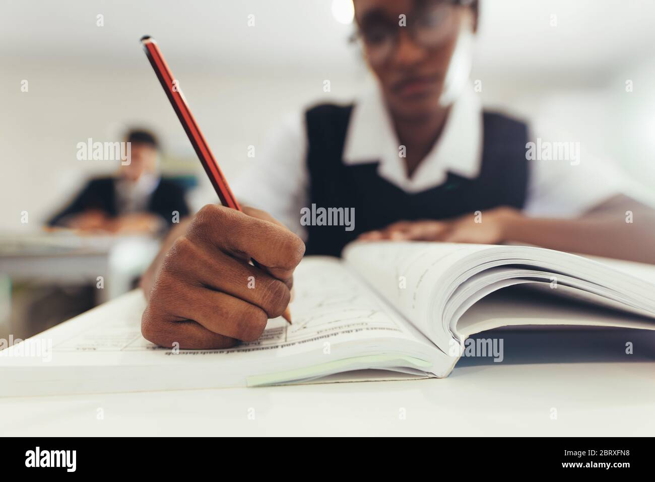 Close-up of a teenage girl writing in her textbook while sitting at desk in classroom. High school student concentrating while writing in a book, focu Stock Photo