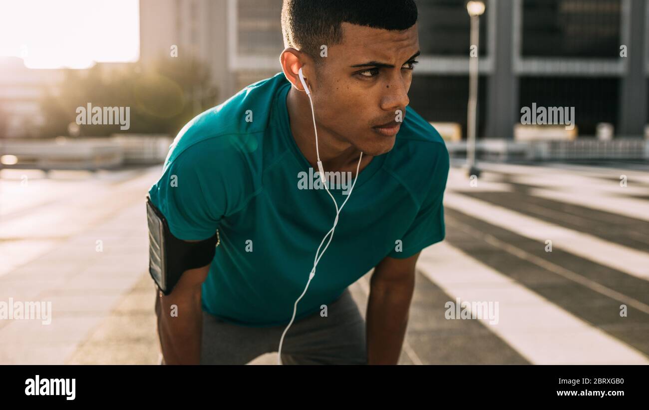 Sportsman standing bent over and resting after a running session in city. Fitness man taking break after a run. Stock Photo