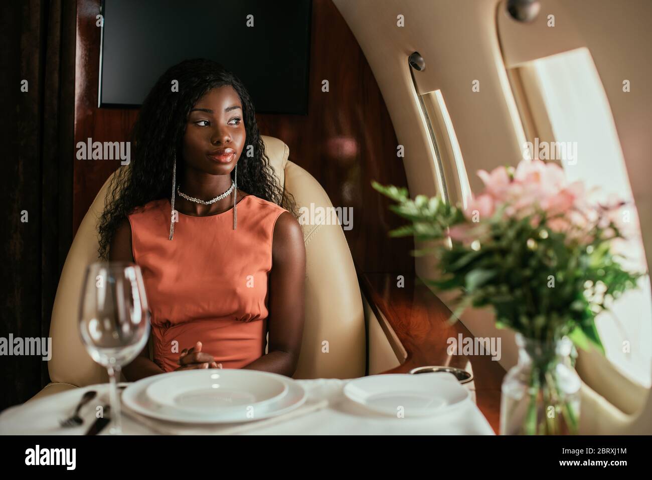 selective focus of dreamy african american woman sitting at served table in private plane Stock Photo