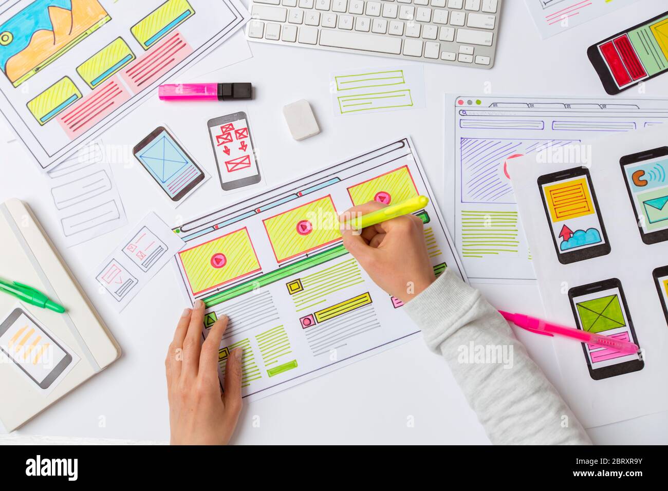 A website designer is working on an application interface. The developer draws sketches of user applications for smartphones. Stock Photo