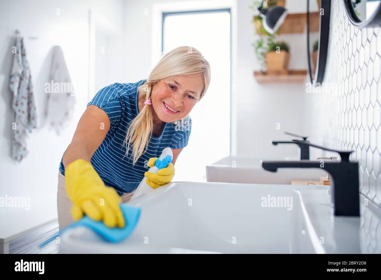 Senior woman with gloves cleaning bathroom indoors at home. Stock Photo