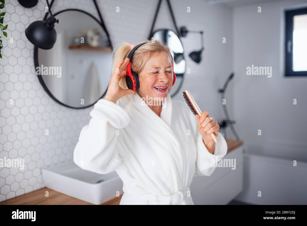 Portrait of senior woman with headphones and bathrobe indoors at home. Stock Photo