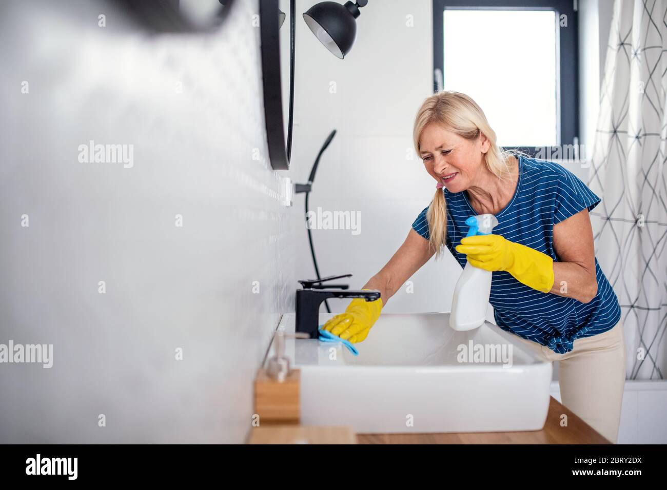 Senior woman with gloves cleaning bathroom indoors at home. Stock Photo