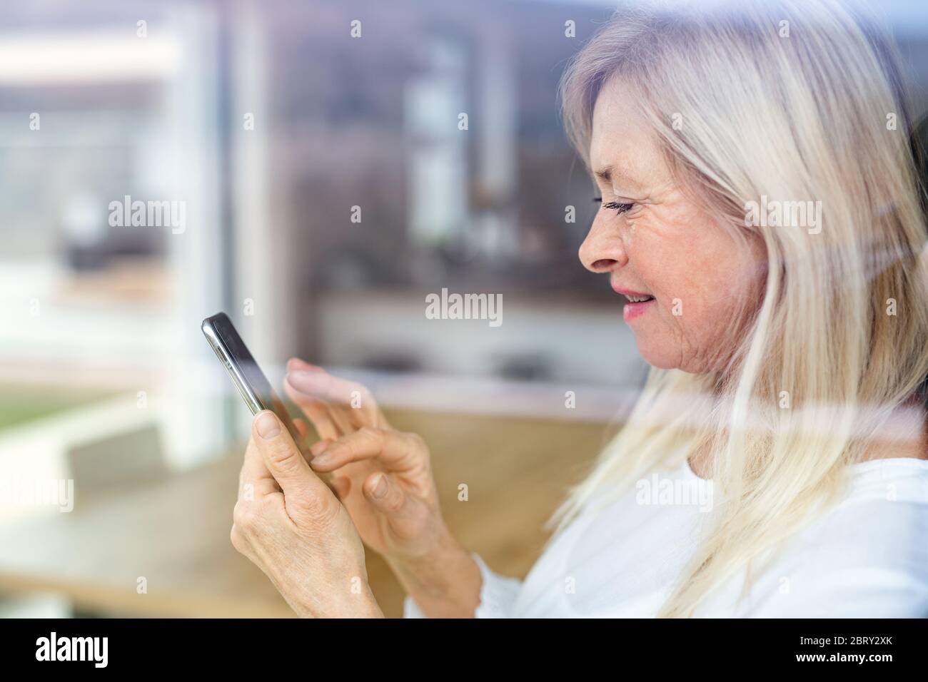 Portrait of senior woman standing indoors at home, using smartphone. Stock Photo