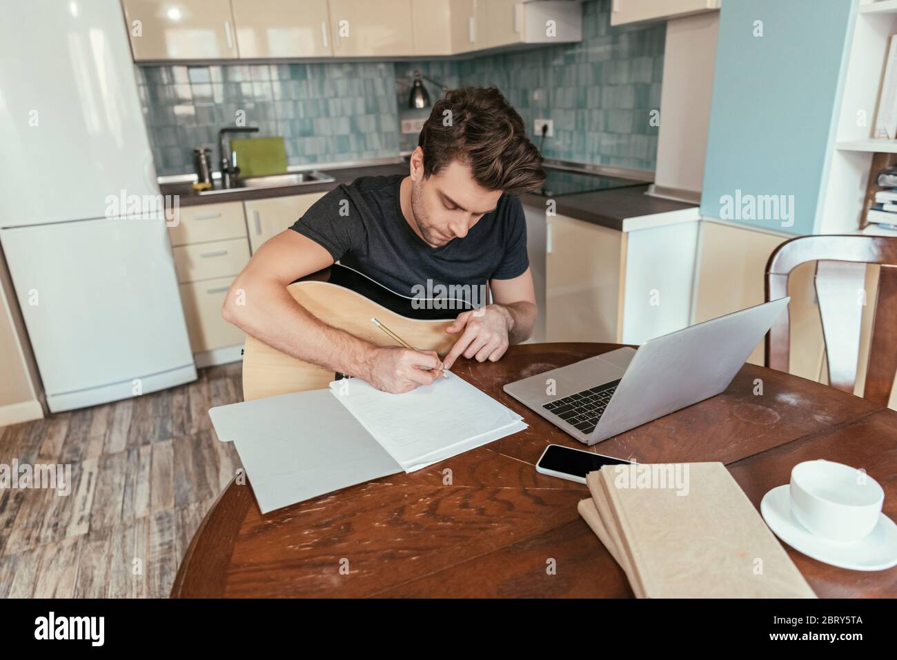 high angle view of attentive young man with guitar writing on paper while sitting near laptop Stock Photo