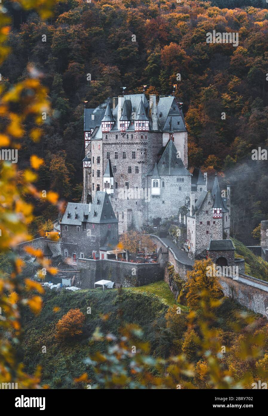 Burg Eltz / Castle Eltz during sunset on a misty autumn day with orange trees and leaves and fog rolling through the valley (Wierschem, Germany, Europ Stock Photo