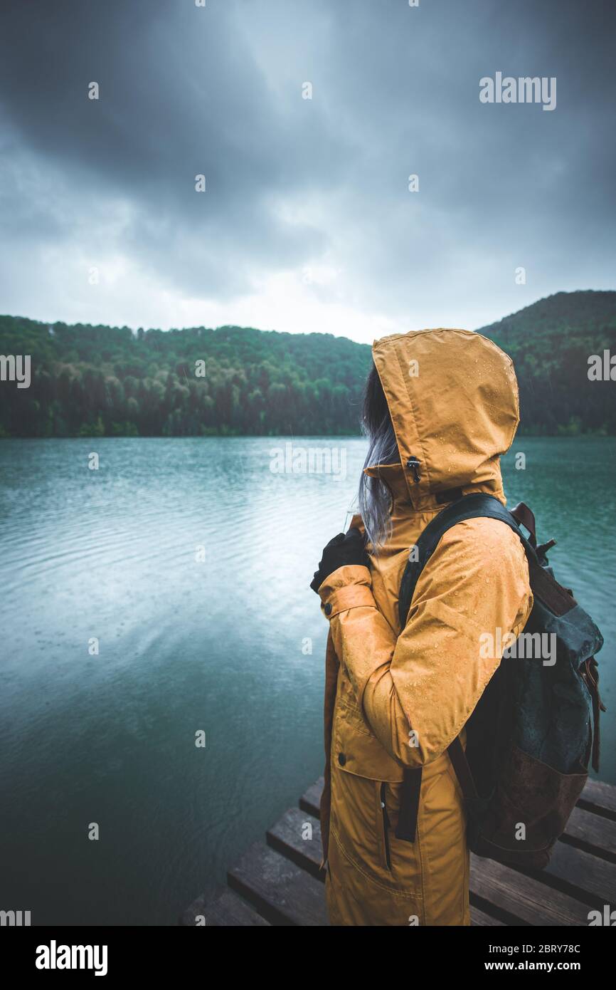 Active outdoors people lifestyle - view of a woman hiker standing on pier in the rain on mountain hike - Outdoors adventure trek activity, wearing wat Stock Photo