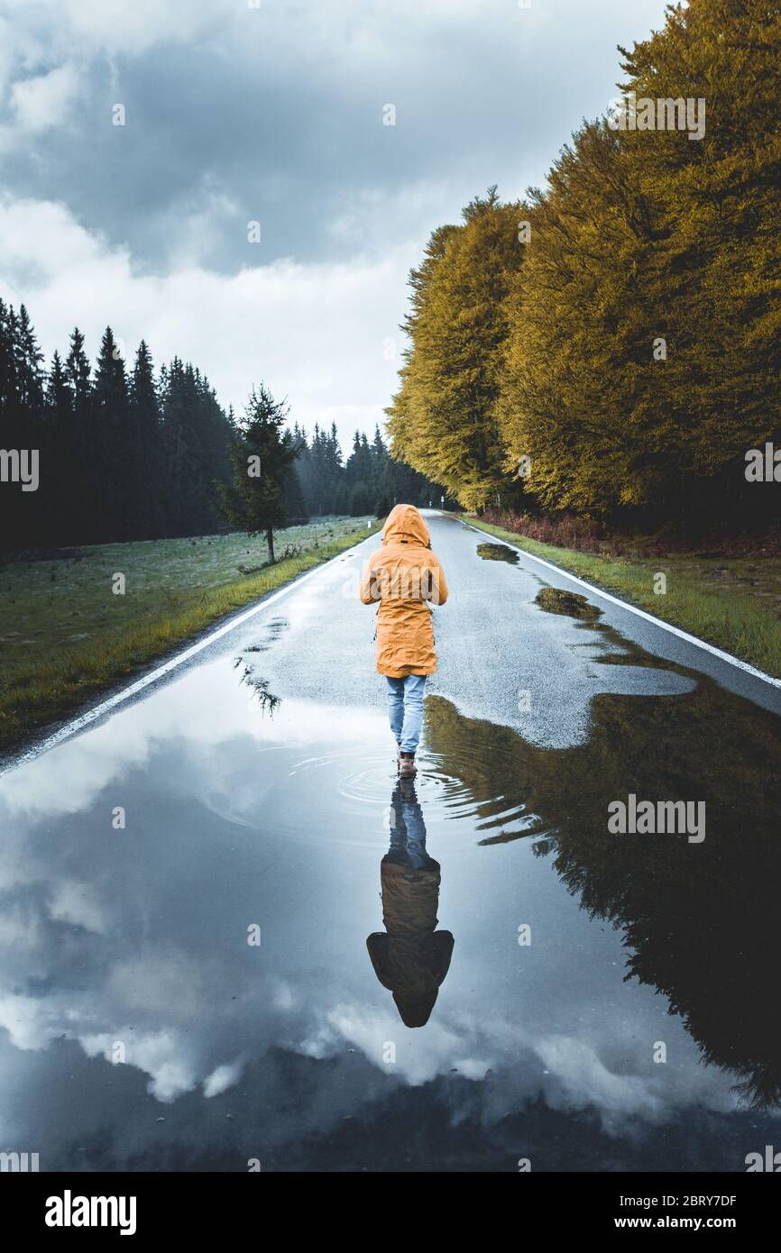 Walking alone concept. Rear view of a woman hiker wearing a yellow jacket walking alone on mountain highway in summer foggy day in Transylvania, Roman Stock Photo