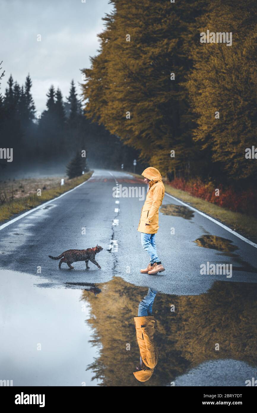 Photo of young woman with her cat walking toward each other. Beautiful reflection over a puddle in Transylvania, Romania Stock Photo