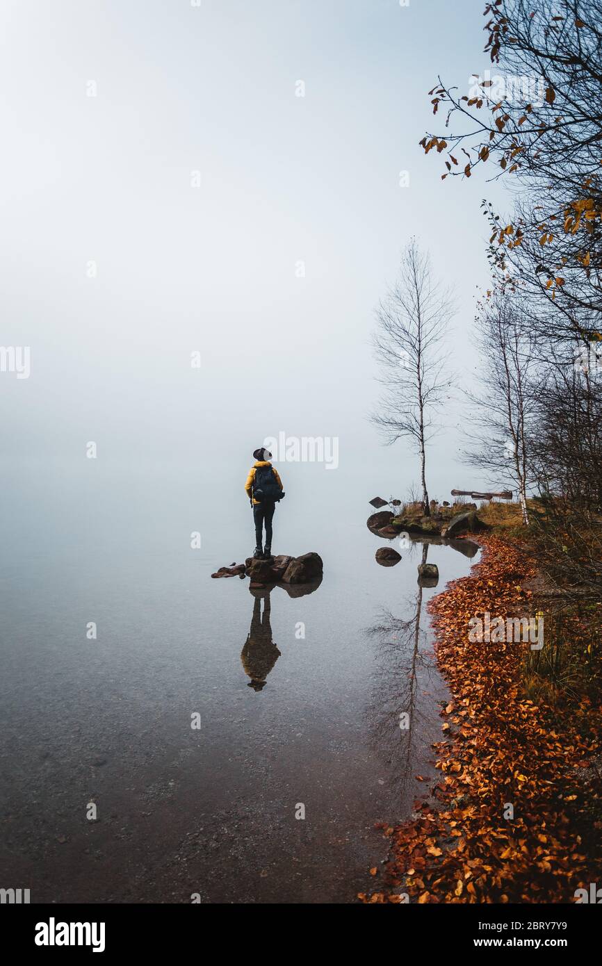 Reflection of a male backpacker standing on rock against foggy weather Stock Photo