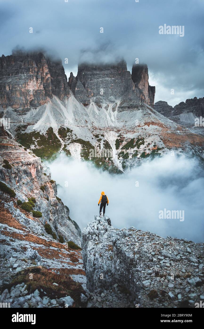Hiker on rock end above valley. Man watch over misty and autumnal morning valley to moody cloudy weather. Tourist looking to misty valley bellow. Autu Stock Photo