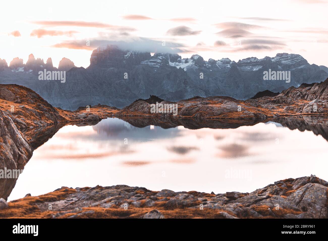 Beautiful landscape with high mountains with illuminated peaks, stones in mountain lake, reflection, blue sky and yellow sunlight in sunrise. Lago Ner Stock Photo