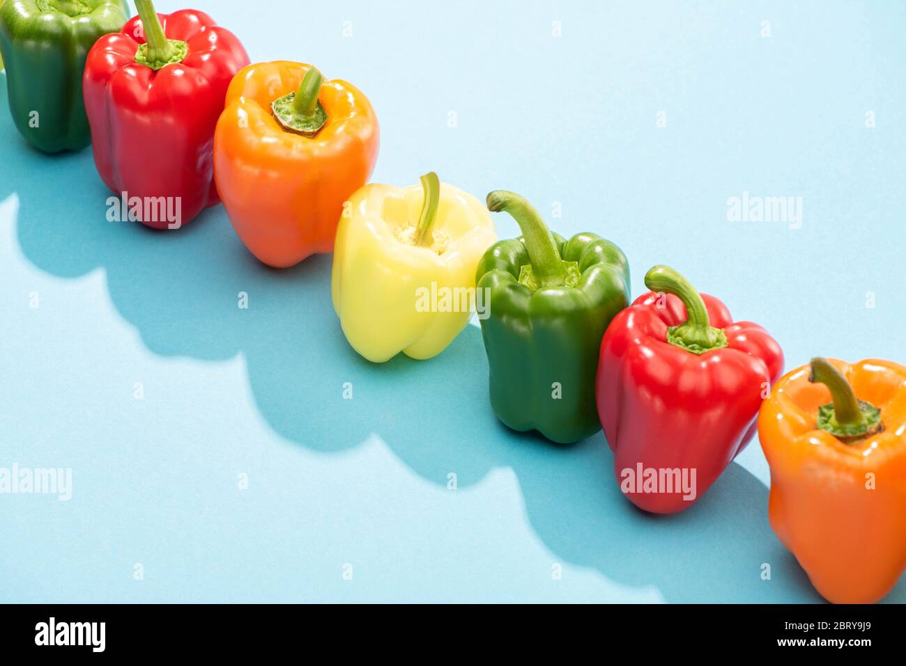 fresh colorful bell peppers in row on blue surface Stock Photo - Alamy