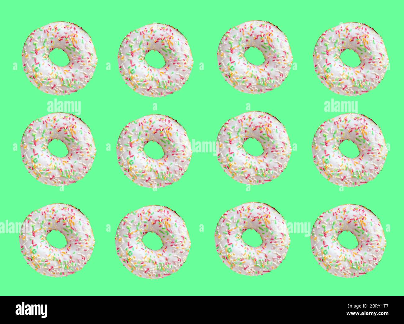 Pattern made of ring donuts with white glaze and clourful hundreds and thousands on green background Stock Photo
