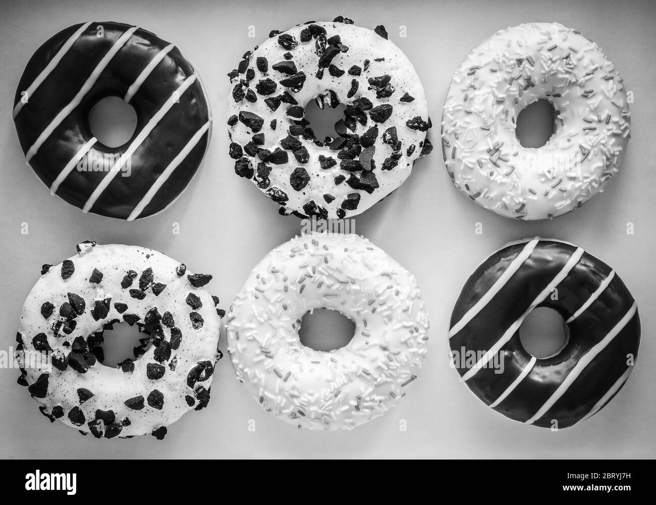 Flat lay image of six ring donuts with white glaze and hundreds and thousands, chocolate and stripes and white glaze with black cookies Stock Photo